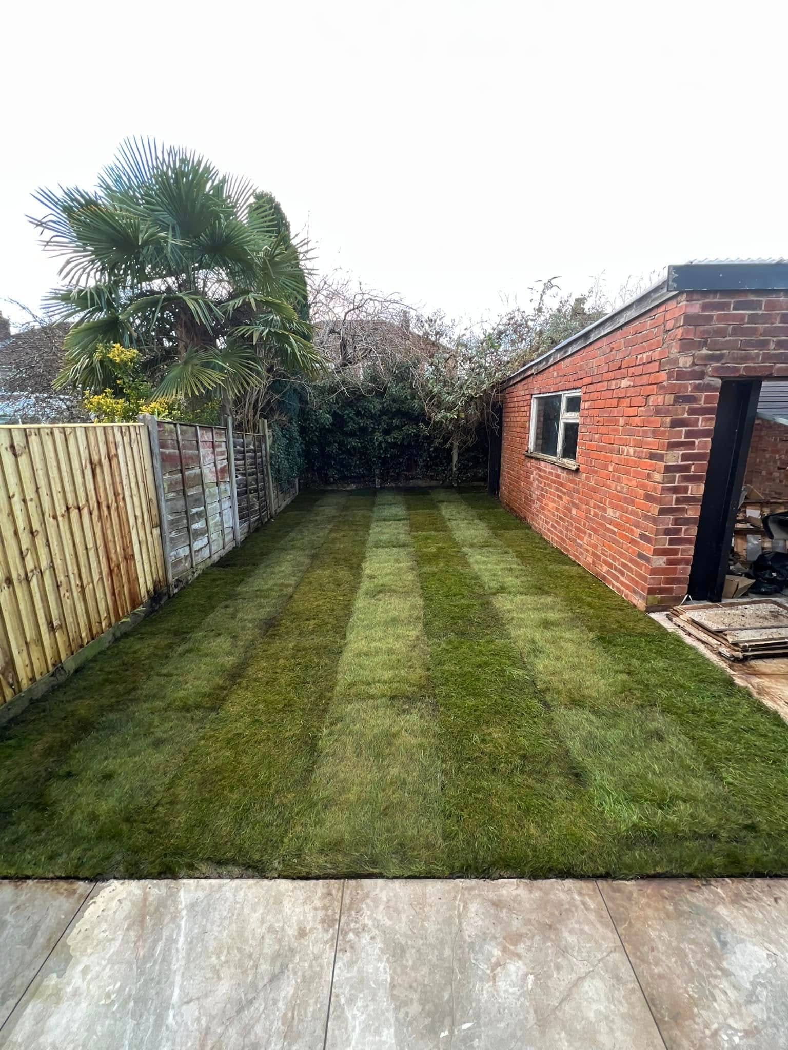 After: striped lawn turf with fencing and brick outbuilding